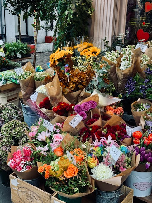 A vibrant display of freshly arranged flower bouquets on a florist's outdoor stand, featuring a variety of flowers including bright yellow sunflowers, soft pink lilies, bold red and purple chrysanthem